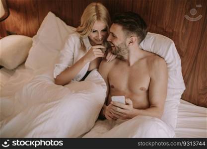 Happy couple in bed at home and use mobile phone