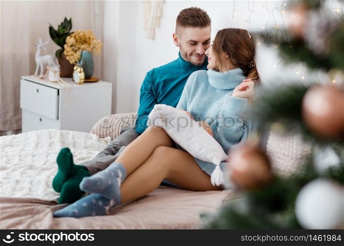 Happy couple in christmas decoration at home. New year eve, decorated fir tree. Winter holiday and love concept.Young happy couple embracing and relaxing on comfortable couch.