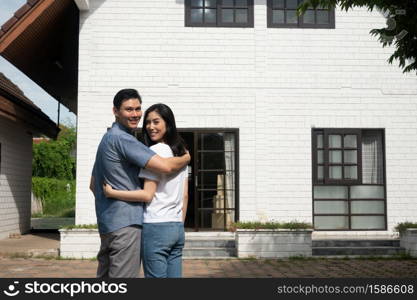 Happy couple in front of the New Home On Moving In Day, and start a new life family. Concept of homeowner and relocation