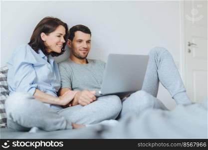 Happy couple in love review their wedding photos on laptop computer, remember plesant moments and special event in their life, use modern laptop computer and free internet connection at home