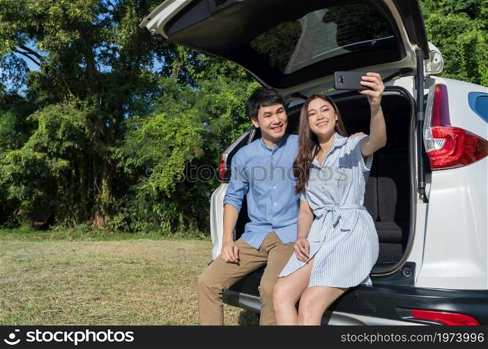 happy couple in love sitting and using smartphone taking a selfie in open car back