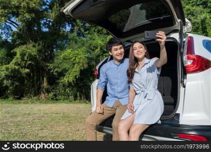 happy couple in love sitting and using smartphone taking a selfie in open car back