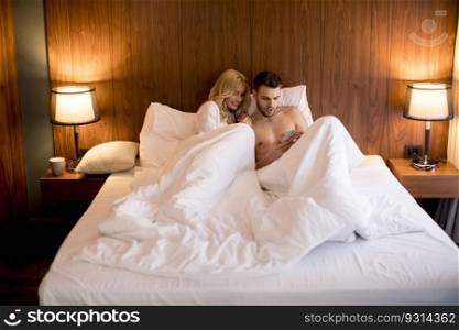 Happy couple in lying in bed at home and use mobile phone