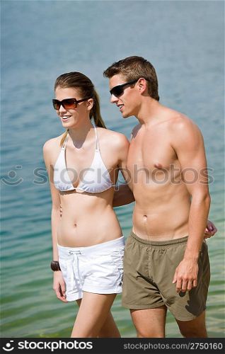 Happy couple in swimwear walk in lake, coastline in background