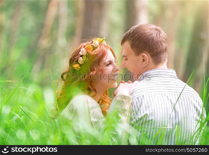 Happy couple in the park, beautiful bride and handsome groom sitting on fresh green grass and talking, love and happiness in wedding day