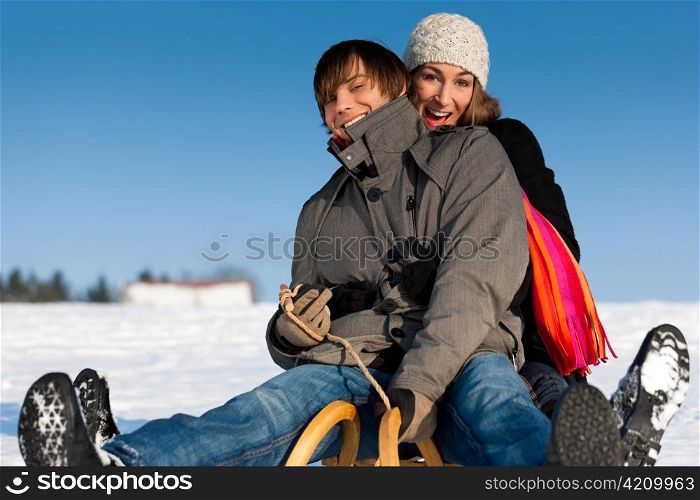 Happy couple in winter sitting on sled in the snow