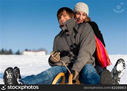 Happy couple in winter sitting on sled in the snow