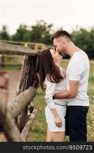 happy couple is kissing near wooden fence. young man and woman are having fun outdoors on a warm summer day. happy couple is kissing near wooden fence. young man and woman are having fun outdoors on a warm summer day.