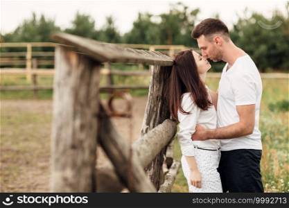 happy couple is kissing near wooden fence. young man and woman are having fun outdoors on a warm summer day. happy couple is kissing near wooden fence. young man and woman are having fun outdoors on a warm summer day.