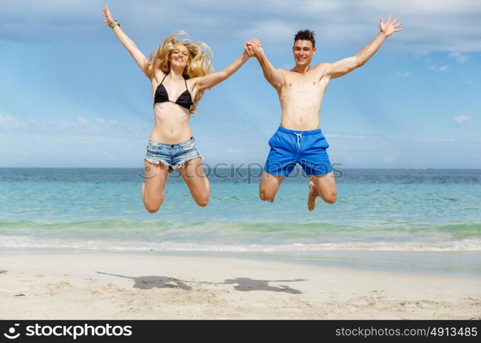 Happy couple jumping on beach vacations. Travel concept of young couple cheering for summer holidays on beach