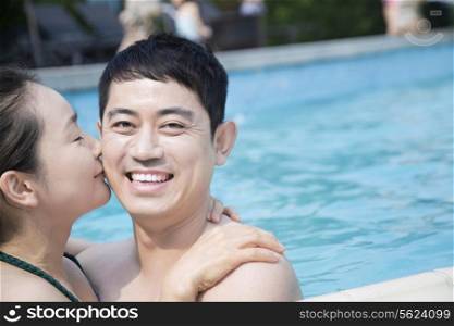 Happy couple kissing and looking at camera in the pool