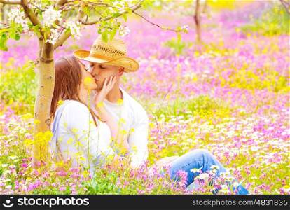 Happy couple kissing outdoors, young family having fun on floral field, spending time together in summer garden, love concept
