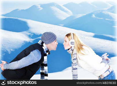 Happy couple kissing, side view face portrait, outdoor at winter snowy mountains, people over natural blue wintertime landscape background, Christmas vacation holidays, love concept