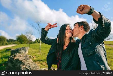 Happy couple kissing while taking a selfie with a smartwatch outdoors. Couple kissing and taking a selfie with a smartwatch