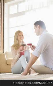 Happy couple looking at each other while having red wine at home