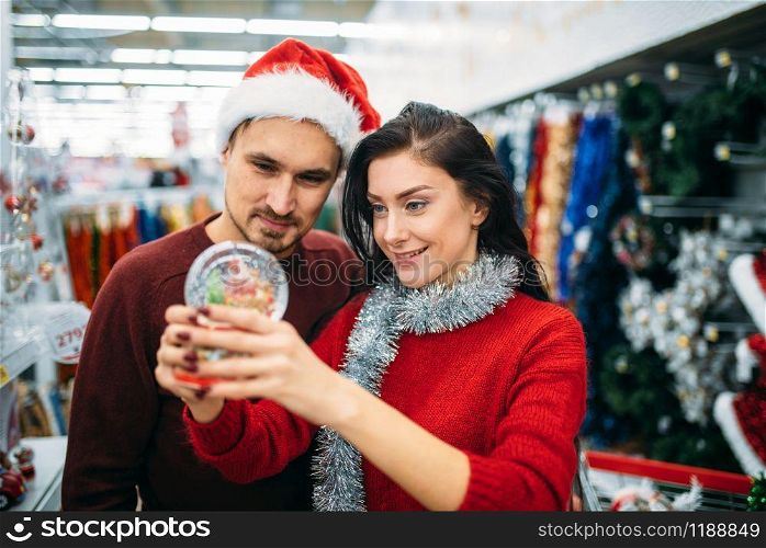 Happy couple looks on christmas snow globe in supermarket, family tradition. December shopping of holiday goods and decorations