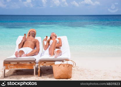 Happy couple on beach resort, tanning on sunbed and eating tasty sweet ice cream, enjoying summer time on beautiful sandy coast