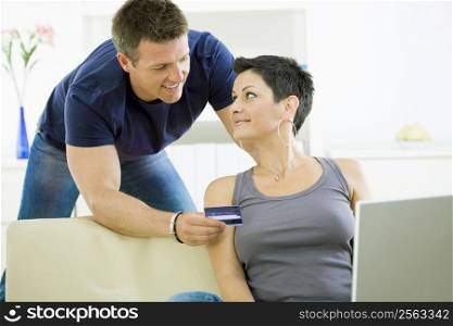 Happy couple paying with credit card at home, smiling.