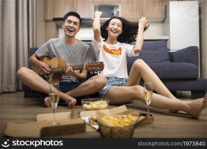 Happy couple playing guitar in the living room