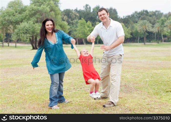 Happy couple playing on the green park with their beautiful daughter over natural background