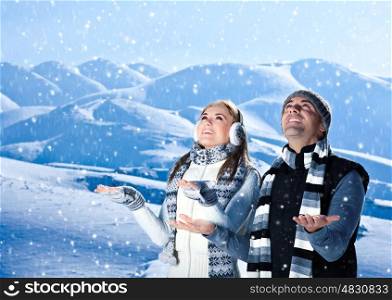 Happy couple playing outdoor at winter mountains, active people over natural blue wintertime landscape background with falling snow, Christmas vacation holidays