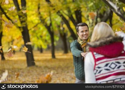 Happy couple playing with autumn leaves in park