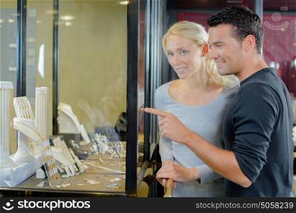 happy couple pointing finger to shopping window at jewelry store