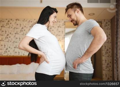Happy couple, pregnant wife with belly at home, bedroom interior on background. Pregnancy, prenatal period. Expectant mom and dad are resting on sofa, health care. Happy couple, pregnant wife with belly at home