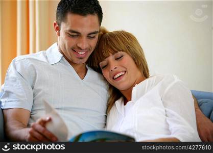 Happy couple reading a magazine on a sofa