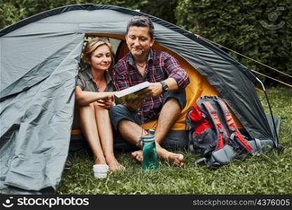 Happy couple relaxing in tent at camping during summer vacation. Man and woman planning next trip looking at map. Actively spending vacations outdoors close to nature. Concept of camp life