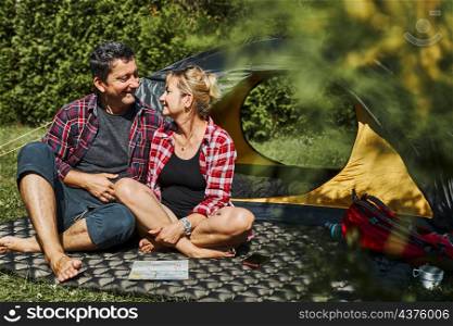 Happy couple relaxing in tent at camping during summer vacation. Man and woman planning next trip with map. Actively spending vacations outdoors close to nature. Concept of camp life