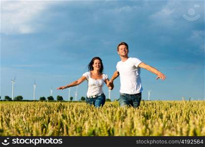 Happy couple running over grainfield in summer hand in hand