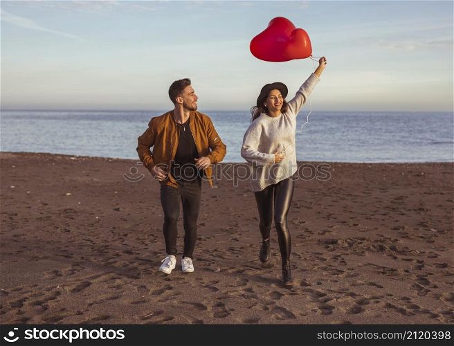 happy couple running sea shore with heart balloons