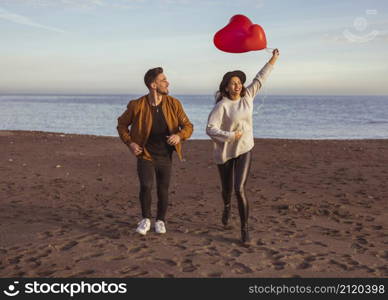 happy couple running sea shore with heart balloons