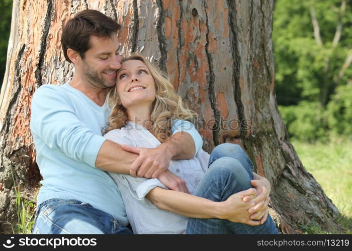 Happy couple sat by tree