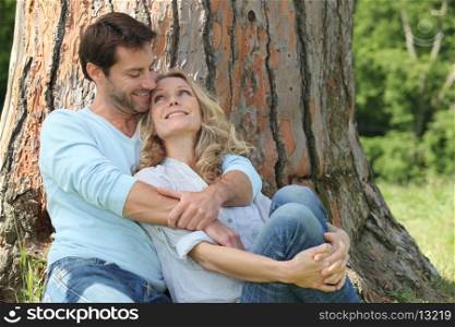 Happy couple sat by tree