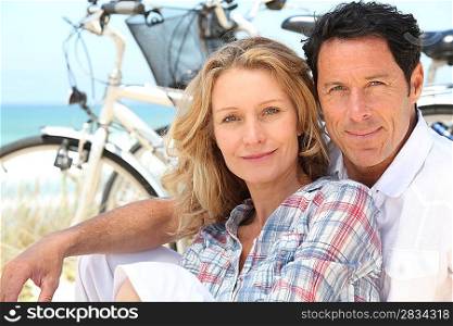 Happy couple sitting by the beach with their bikes