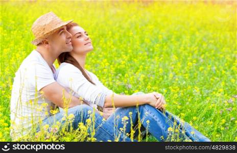 Happy couple sitting down on fresh yellow floral field, romantic date, hugging outdoors, loving family, romance and enjoyment concept