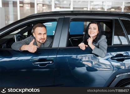 Happy couple sitting in new car, showroom. Male and female customers choosing vehicle in dealership, automobile sale, auto purchase