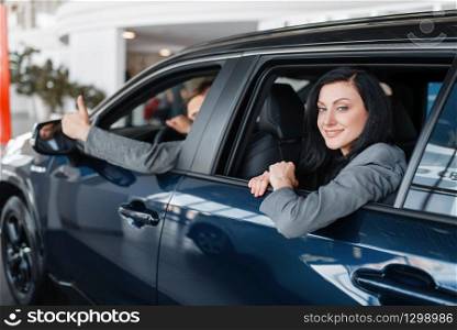 Happy couple sitting in new car, showroom. Male and female customers choosing vehicle in dealership, automobile sale, auto purchase. Happy couple sitting in new car, showroom