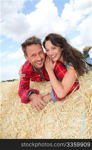 Happy couple sitting on bale in farmland