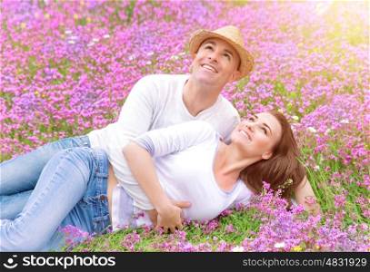 Happy couple spending time outdoors, lying down and hugging on beautiful pink floral field, romantic relationship, love concept