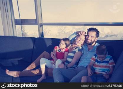 happy couple spending time with kids using tablet computer on sofa at home. happy young couple spending time with kids at home