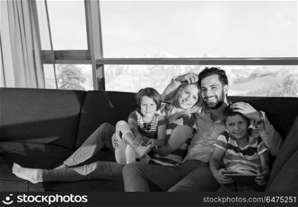 happy couple spending time with kids using tablet computer on sofa at home. happy young couple spending time with kids at home