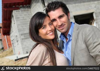 Happy couple standing in front of house under construction