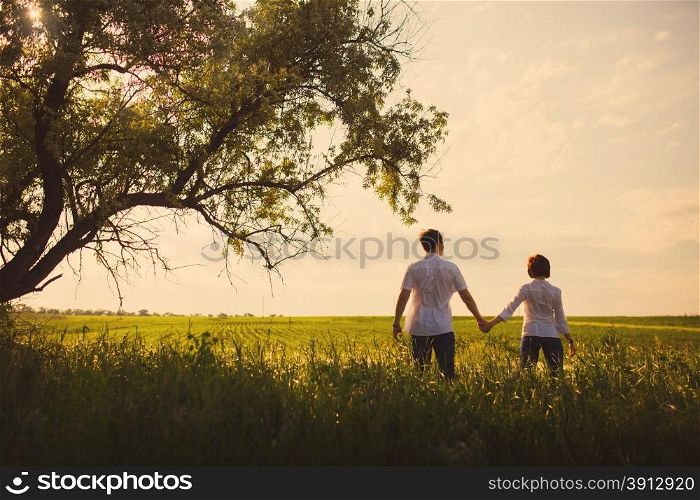 Happy couple standing in the field at the sunset, tinted photo