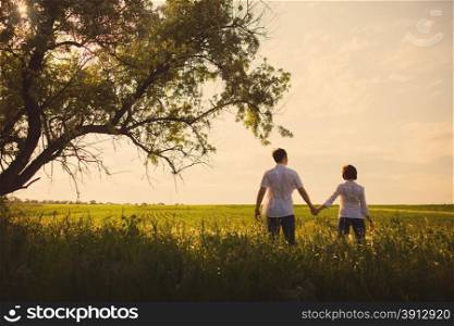 Happy couple standing in the field at the sunset, tinted photo