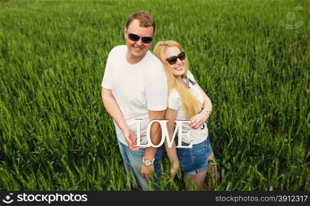 Happy couple standing in wheat field with love word in hands