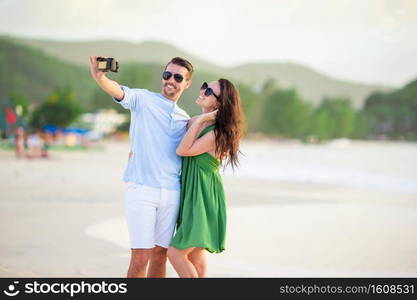 Happy couple taking a selfie photo on white beach. Two adults enjoying their vacation on tropical exotic beach. Happy couple taking a photo on white beach on honeymoon holiday