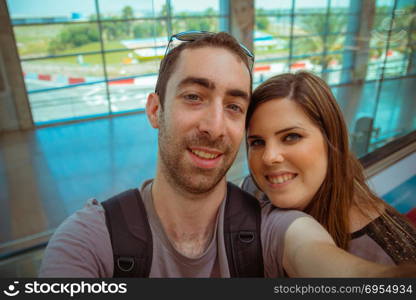 Happy couple taking selfie with smartphone or camera in airport.